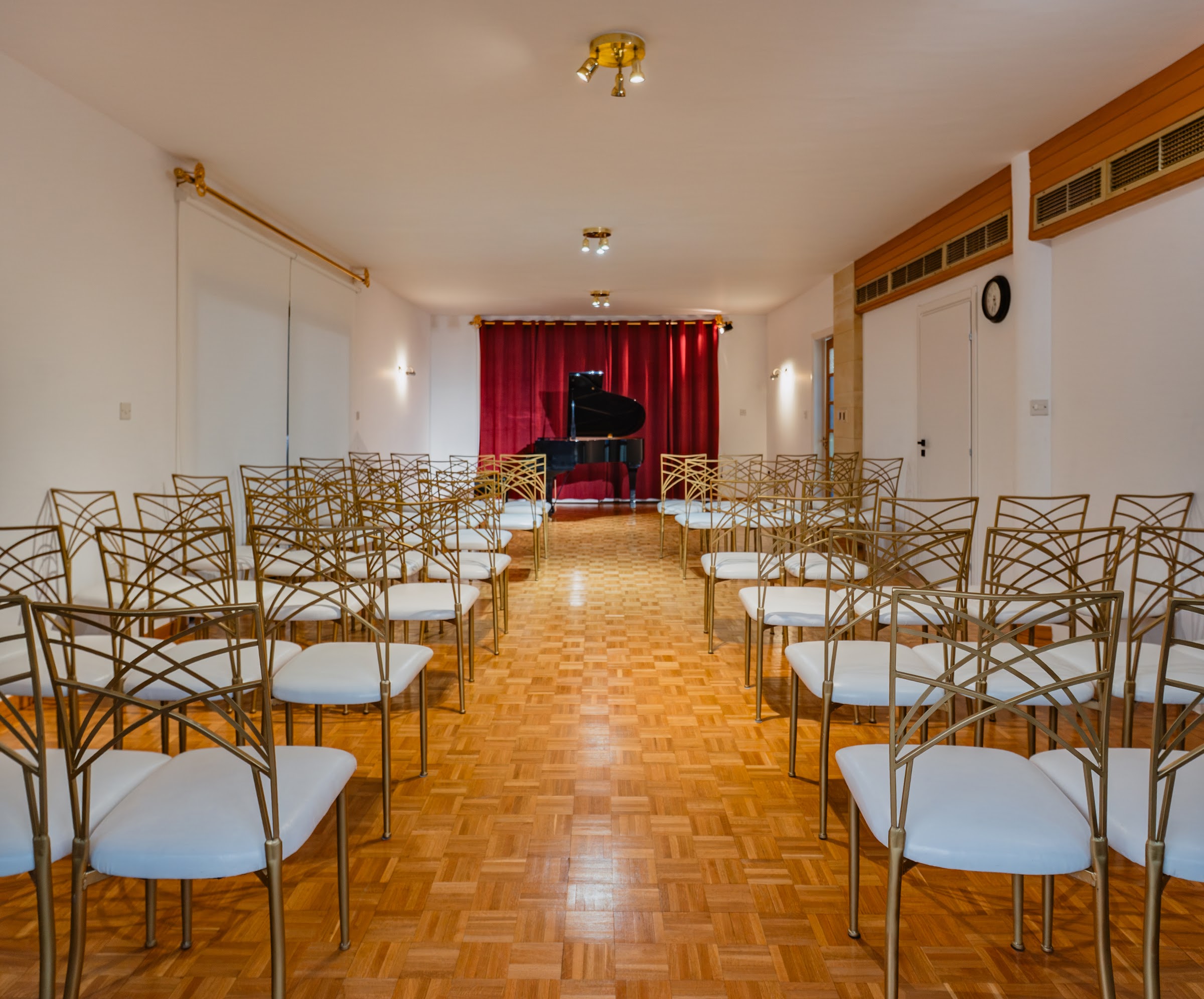 Performance hall from the audience: rows of gold chairs facing the stage, grand piano under red velvet curtain