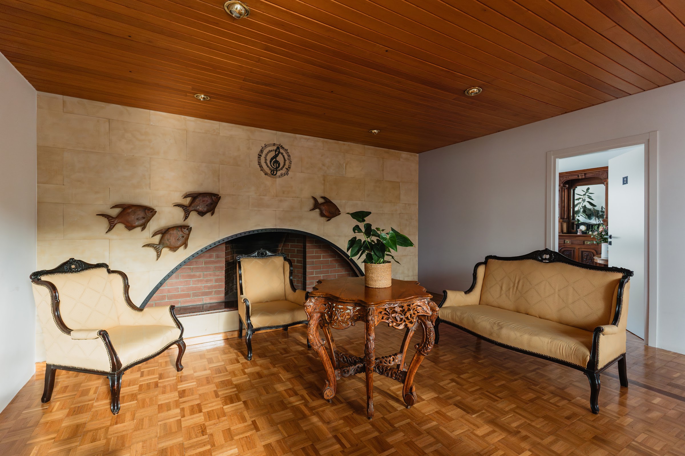 Elegant lounge: ornate fireplace, antique sofas, warm wood ceiling, treble clef wall art