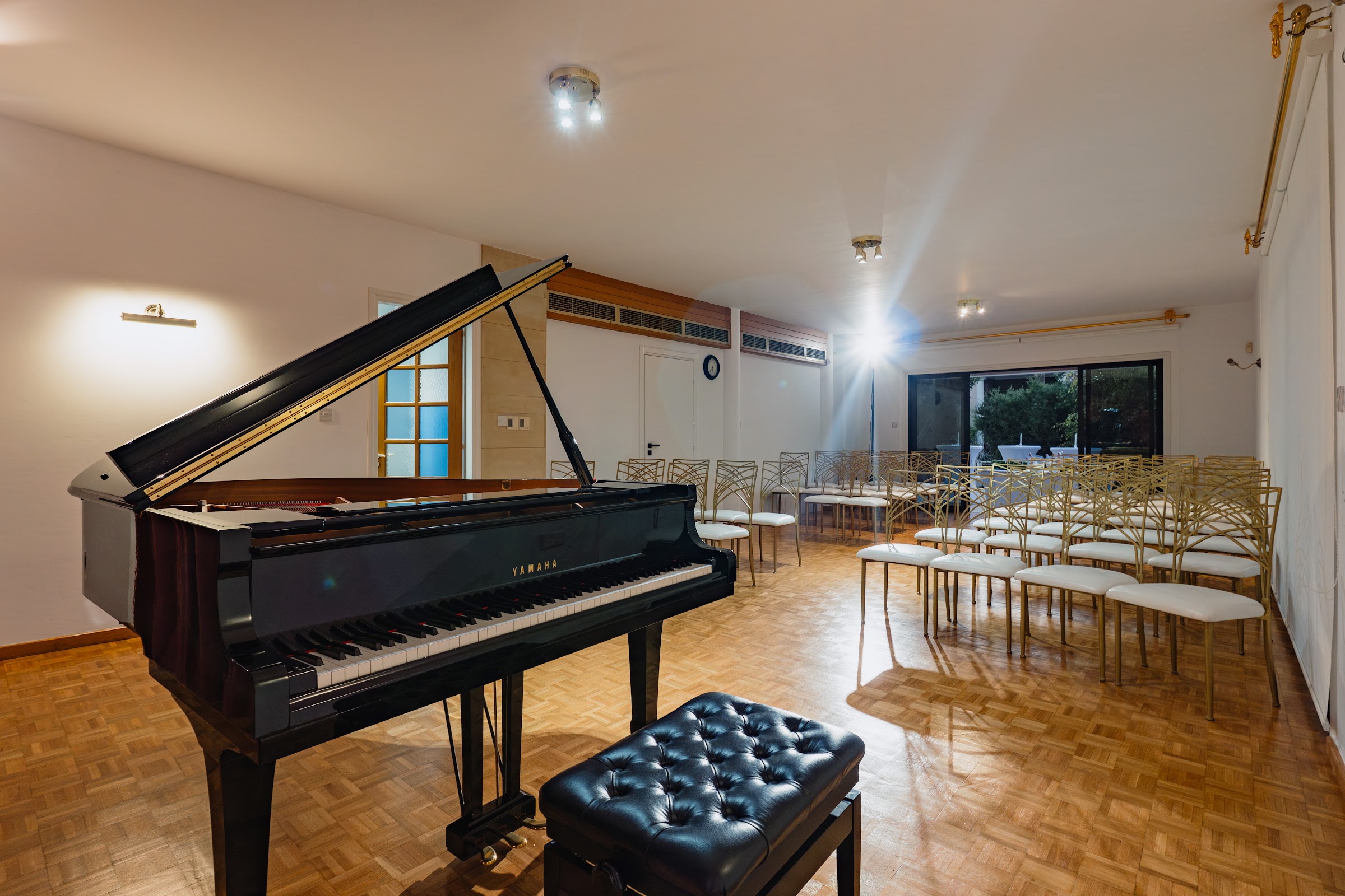 Yamaha grand piano in the performance hall: leather bench, gold seating, warm stage lighting