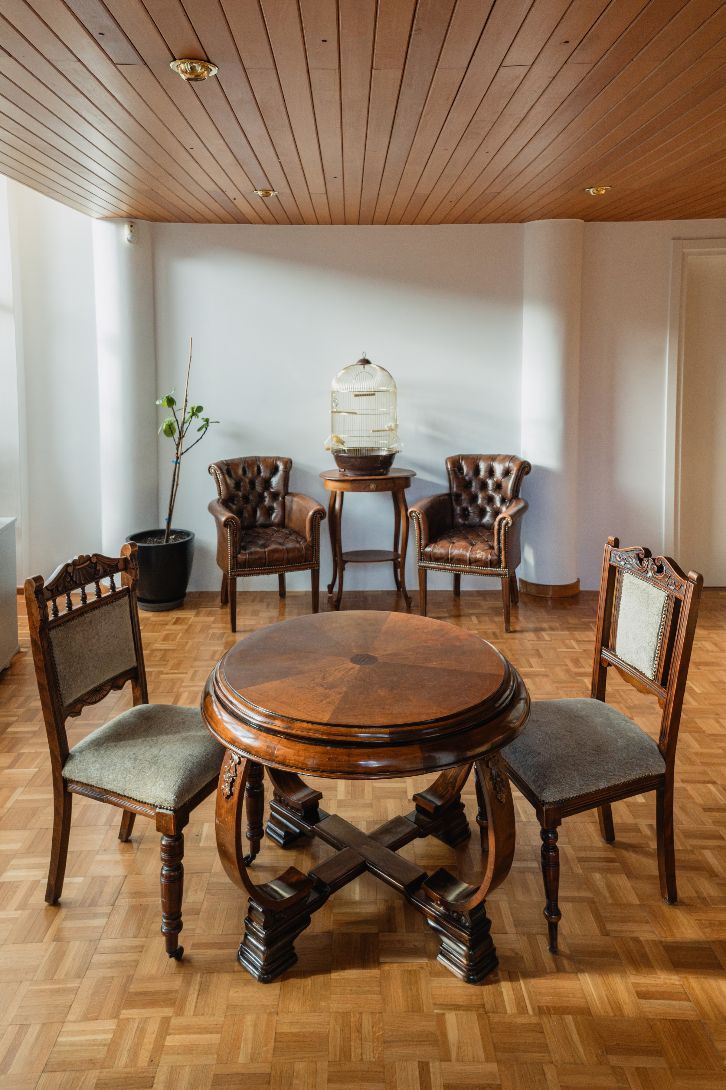 Antique study area: round wooden table, leather Chesterfield chairs, warm wood-panelled ceiling