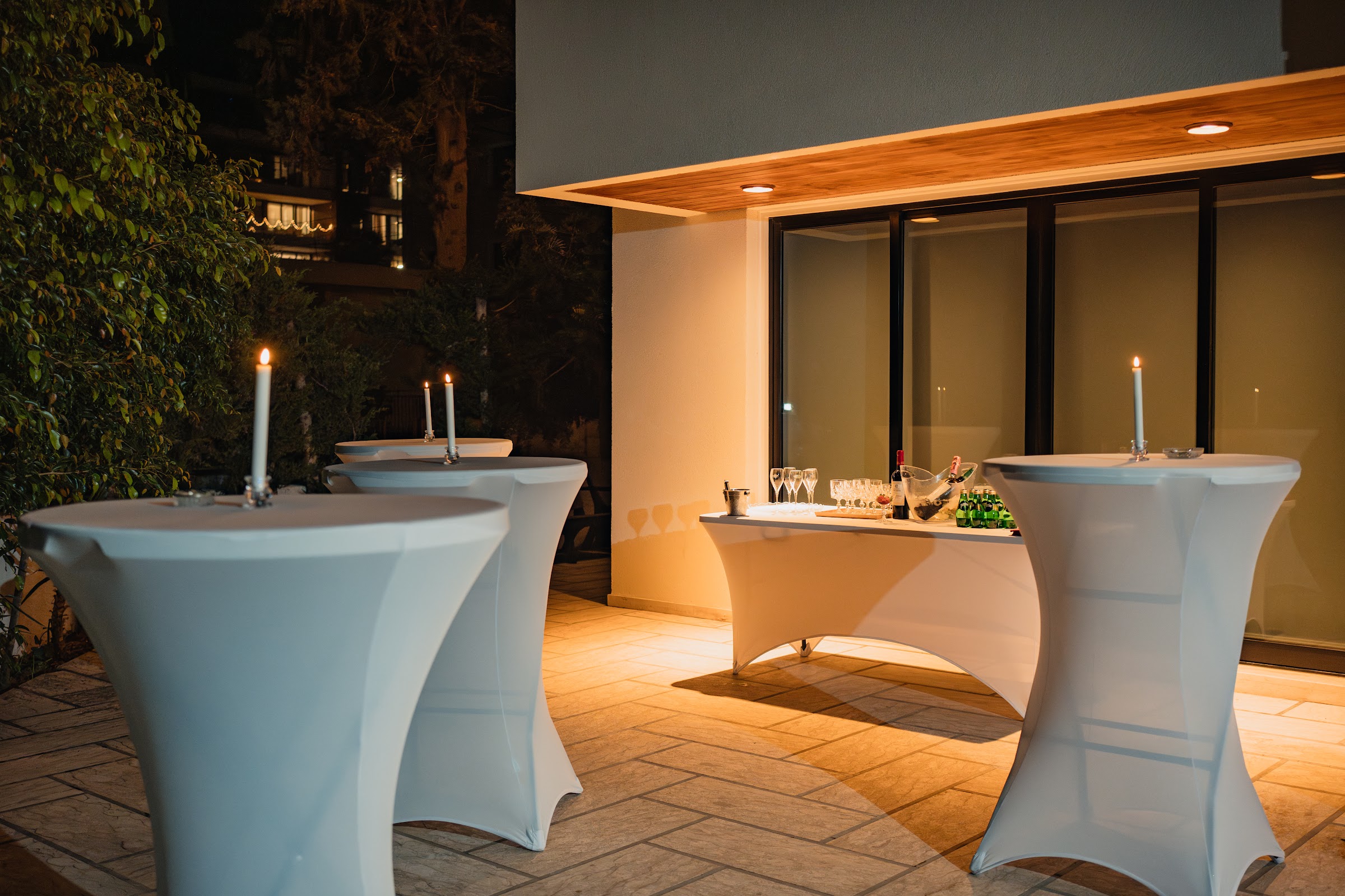 Evening terrace: cocktail tables with candles, champagne service under warm ambient lighting