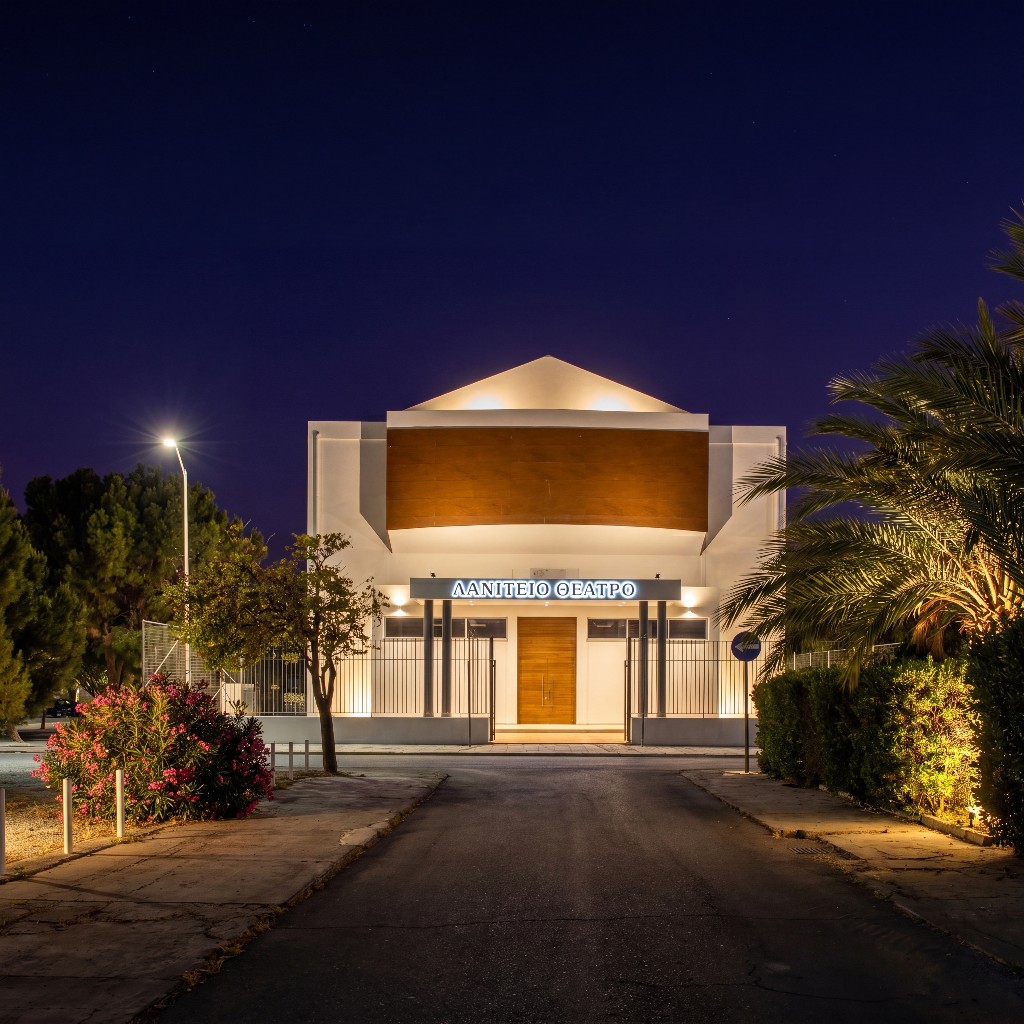 Laniteio Theatre exterior at night: illuminated white façade with bronze cladding, palm-lined approach, Limassol