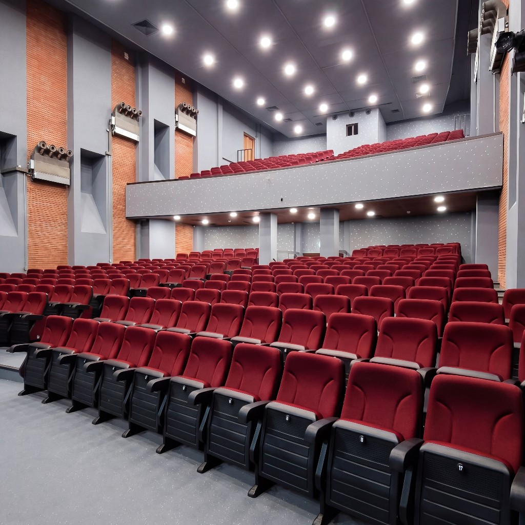 Laniteio Theatre auditorium: rows of red velvet seats, balcony above, recessed stage lighting