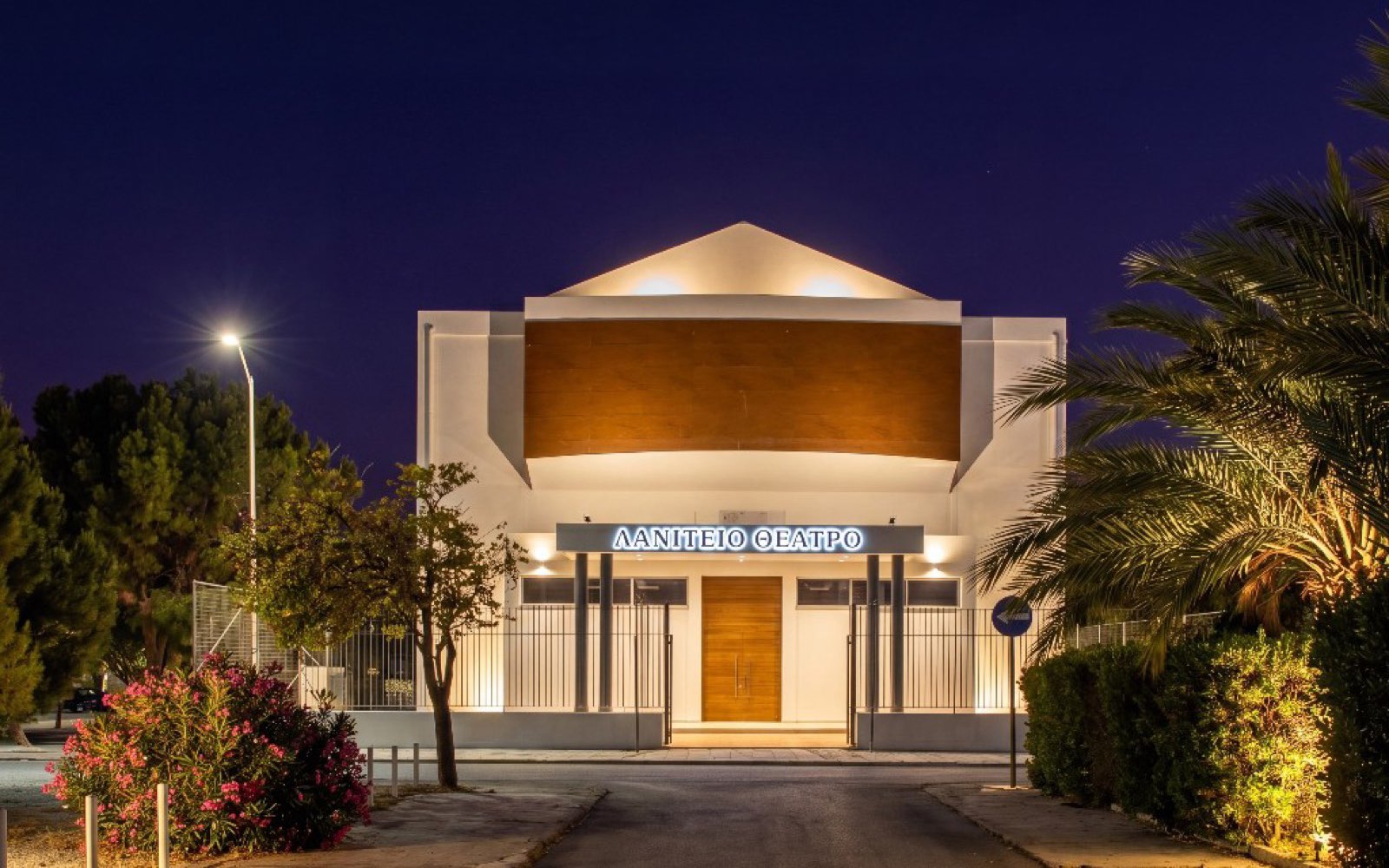 The Laniteio Theatre at night: illuminated façade under an indigo Mediterranean sky, palms alongside