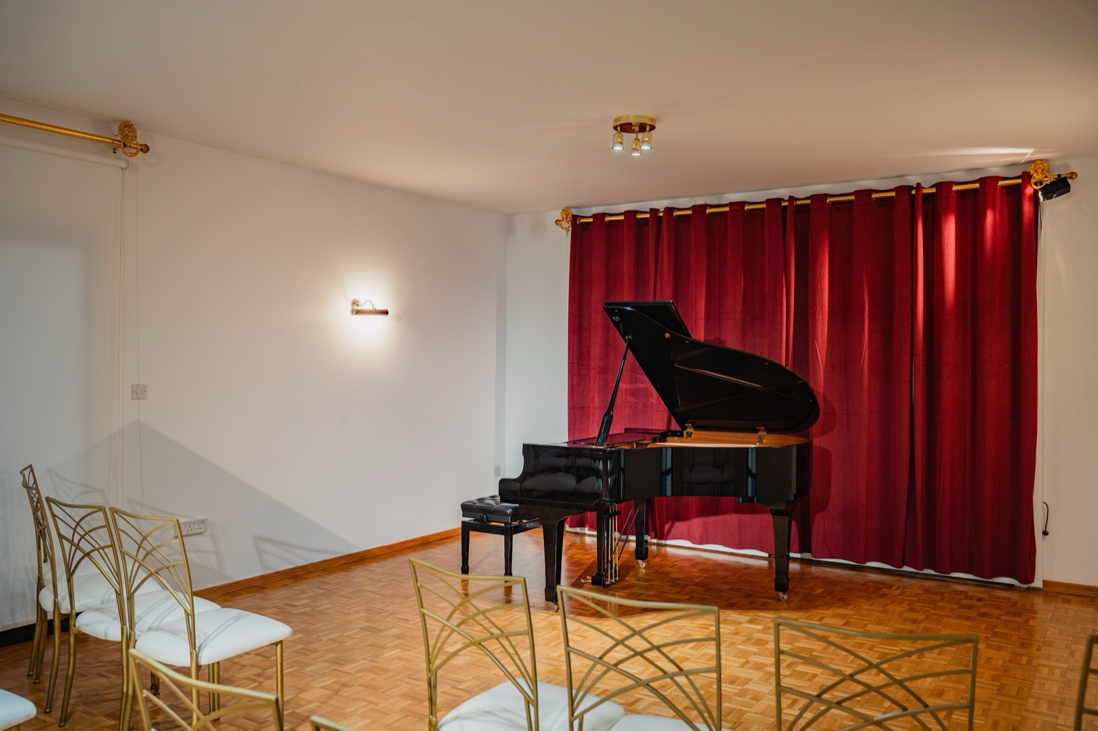 A grand piano, lid open, before a red velvet curtain in the recital hall
